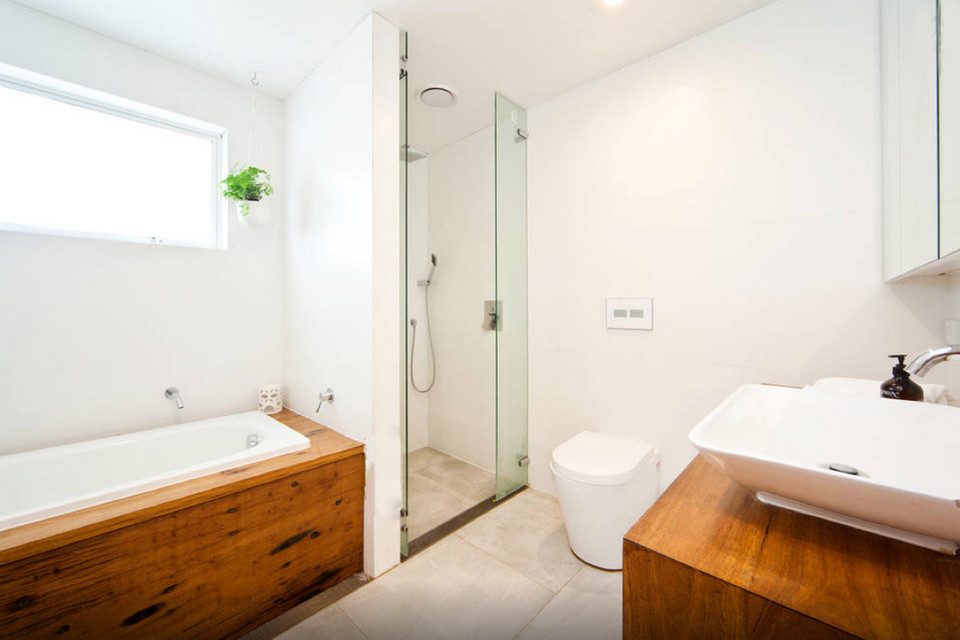 Mid-sized beach style master bathroom in Sydney with a vessel sink, wood benchtops, a drop-in tub, a corner shower, a one-piece toilet, white tile, stone tile, white walls and limestone floors.