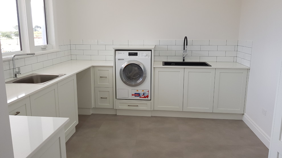 Photo of a large contemporary u-shaped dedicated laundry room in Other with an utility sink, shaker cabinets, white cabinets, quartz benchtops, white walls, ceramic floors, a stacked washer and dryer, grey floor and yellow benchtop.