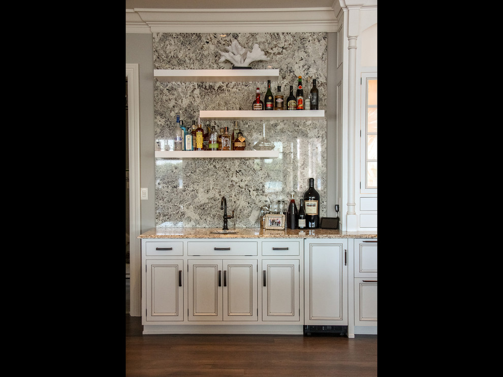 This is an example of a large beach style single-wall wet bar in Other with an undermount sink, beaded inset cabinets, white cabinets, multi-coloured splashback, stone slab splashback, medium hardwood floors, brown floor and multi-coloured benchtop.