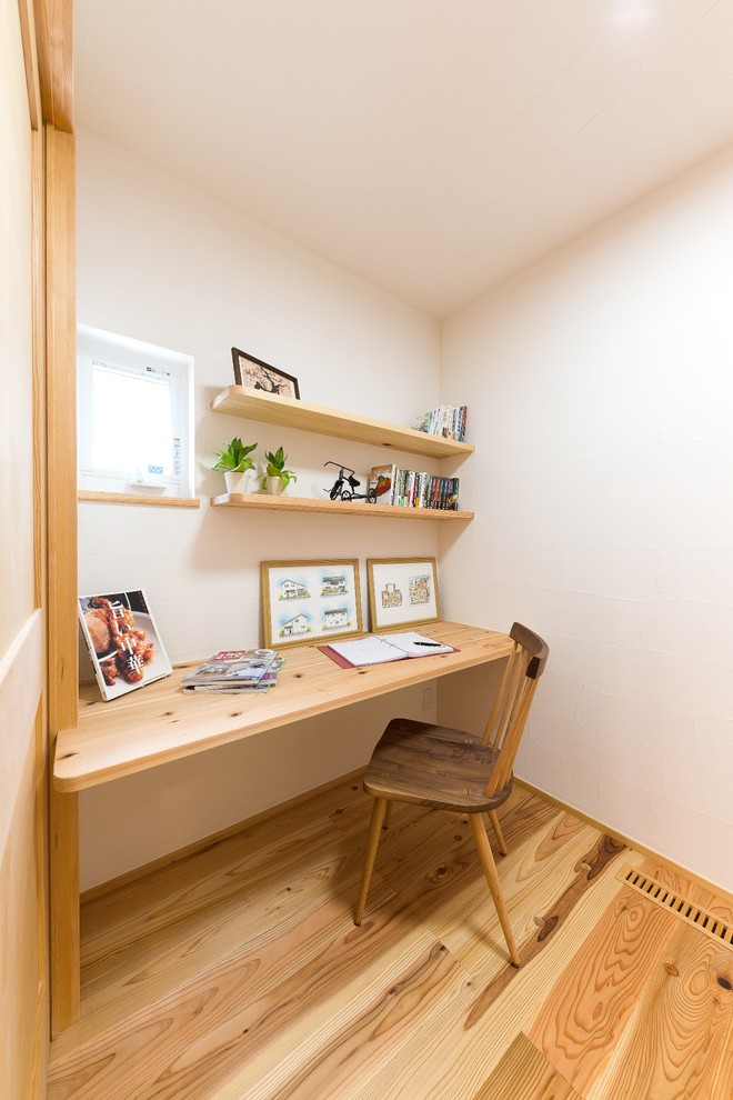 This is an example of an asian home office in Other with white walls, medium hardwood floors, a built-in desk and brown floor.