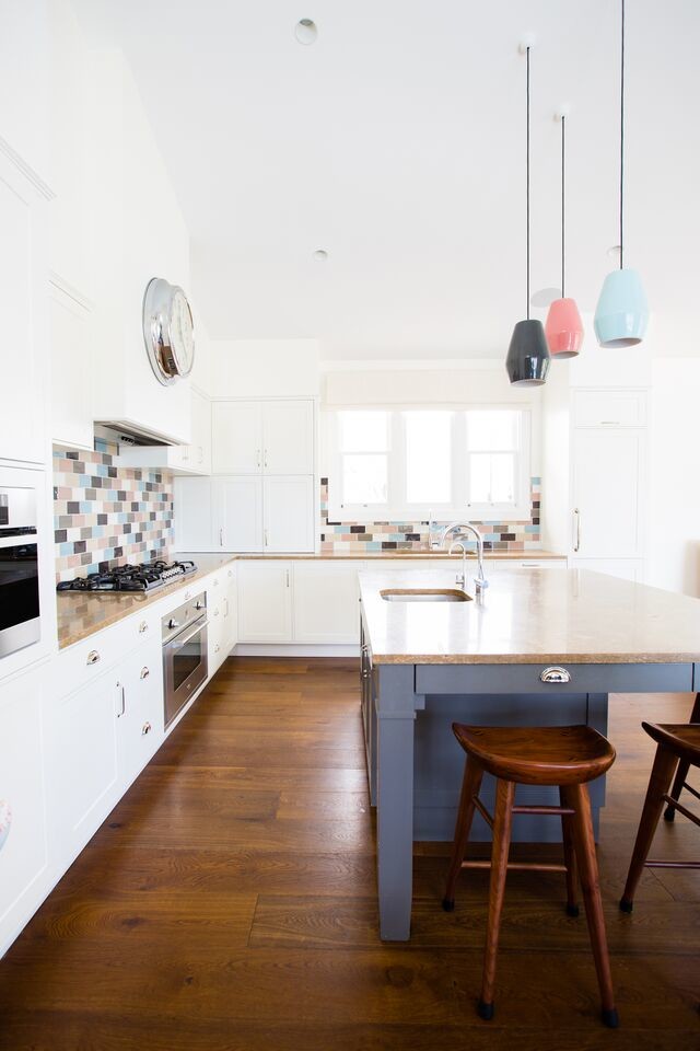 Large modern l-shaped open plan kitchen in Sydney with an undermount sink, shaker cabinets, white cabinets, multi-coloured splashback, stainless steel appliances, medium hardwood floors, with island, limestone benchtops, ceramic splashback and brown floor.