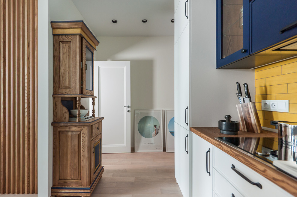 This is an example of an eclectic l-shaped open plan kitchen in Other with a drop-in sink, beaded inset cabinets, white cabinets, wood benchtops, yellow splashback, porcelain splashback, no island and brown benchtop.