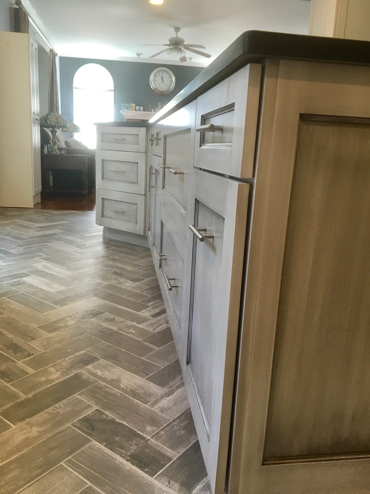 Mid-sized transitional l-shaped eat-in kitchen in Philadelphia with a farmhouse sink, shaker cabinets, white cabinets, granite benchtops, grey splashback, mosaic tile splashback, stainless steel appliances, porcelain floors, with island and grey floor.