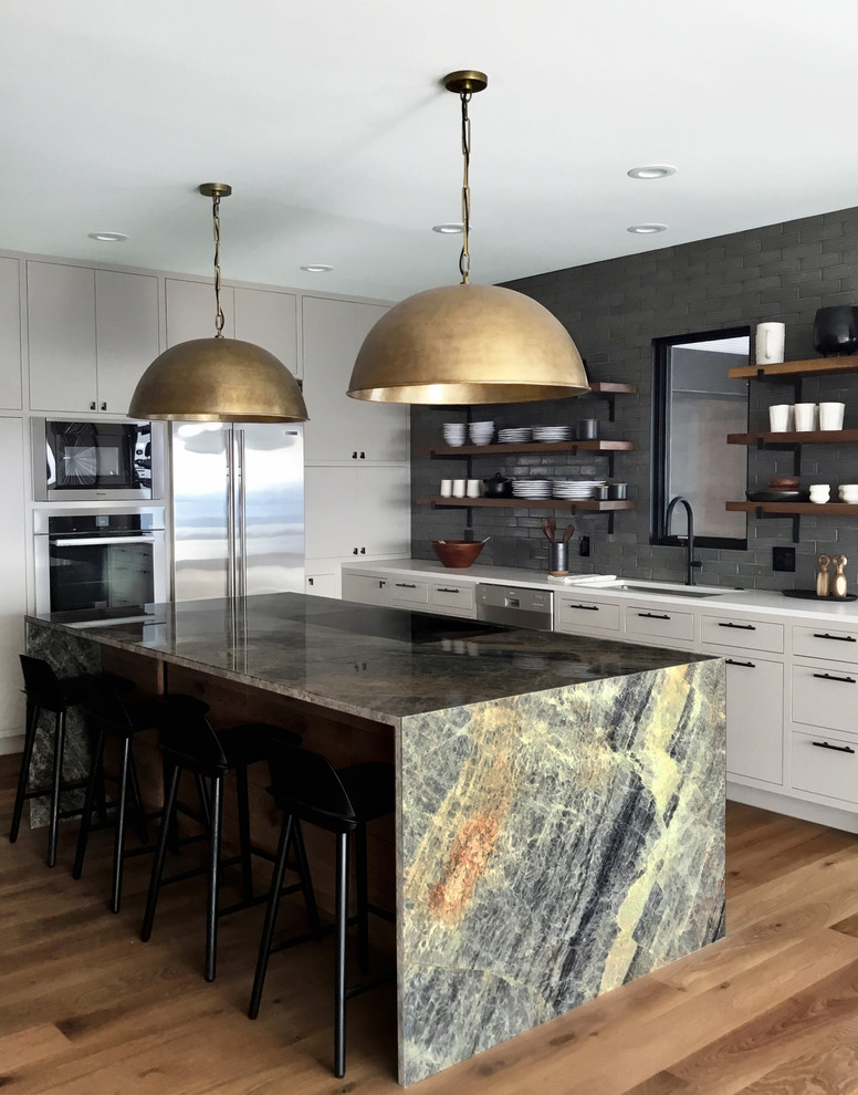 Design ideas for a contemporary l-shaped kitchen in New York with an undermount sink, flat-panel cabinets, white cabinets, grey splashback, subway tile splashback, medium hardwood floors, with island and brown floor.