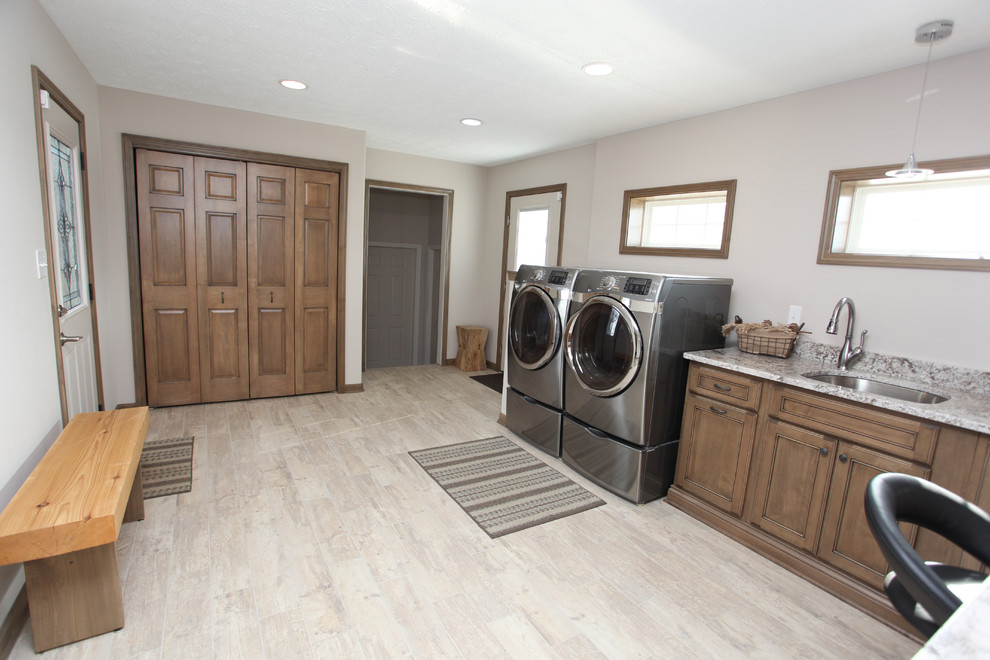 This is an example of a large arts and crafts single-wall dedicated laundry room in Indianapolis with an undermount sink, recessed-panel cabinets, medium wood cabinets, granite benchtops, beige walls, laminate floors, a side-by-side washer and dryer and beige floor.