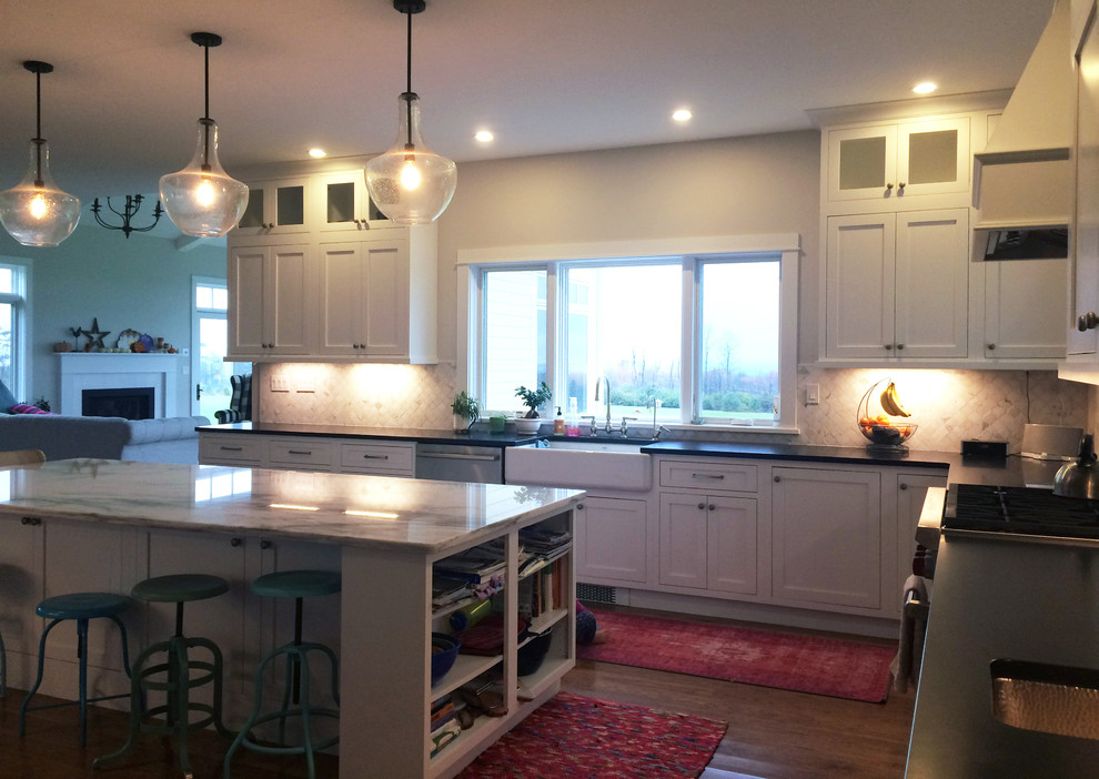 Large transitional l-shaped dark wood floor and brown floor kitchen pantry photo with a farmhouse sink, recessed-panel cabinets, white cabinets, quartz countertops, beige backsplash, ceramic backsplash, stainless steel appliances, an island and black countertops
