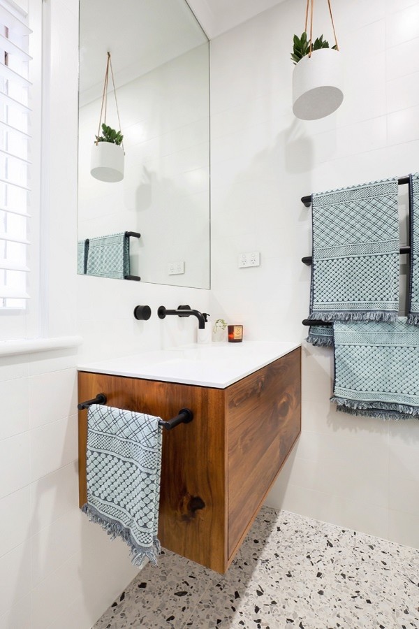 This is an example of a mid-sized modern 3/4 wet room bathroom in Sydney with furniture-like cabinets, dark wood cabinets, a wall-mount toilet, black and white tile, stone tile, white walls, terrazzo floors, an integrated sink, engineered quartz benchtops, multi-coloured floor, a hinged shower door and white benchtops.