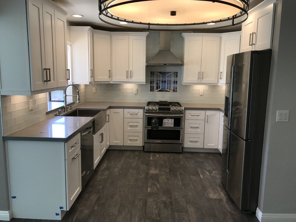 Design ideas for a mid-sized contemporary u-shaped eat-in kitchen in Los Angeles with a farmhouse sink, shaker cabinets, white cabinets, quartzite benchtops, glass tile splashback, stainless steel appliances, ceramic floors, no island, brown floor, grey benchtop and grey splashback.