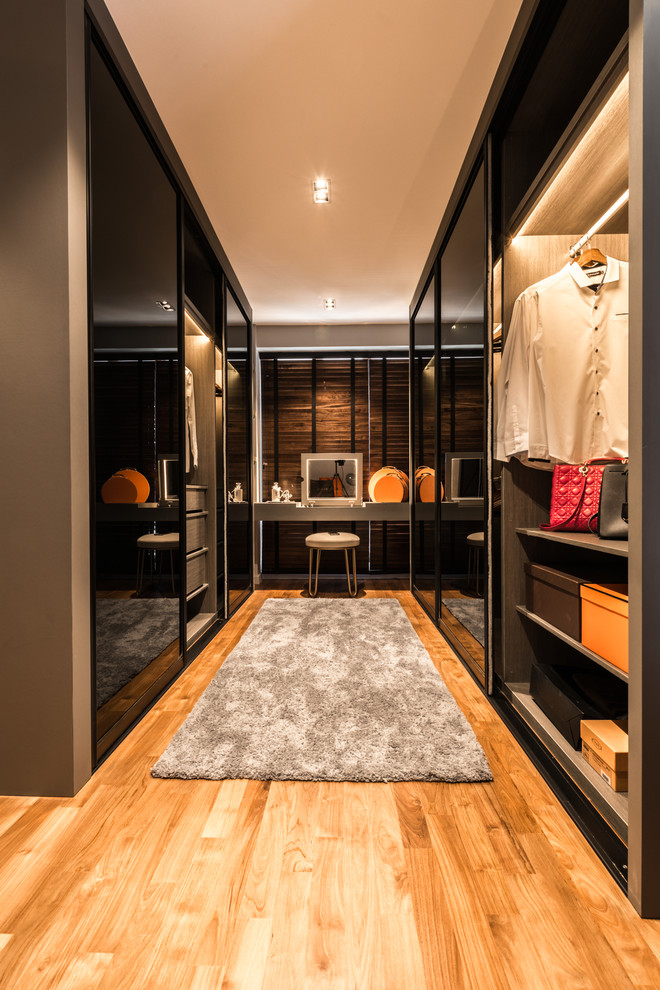 Mid-sized contemporary women's dressing room in Singapore with flat-panel cabinets and medium hardwood floors.