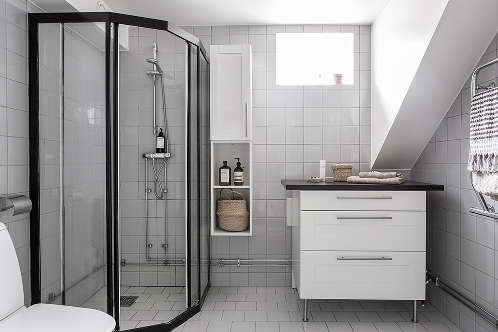 Design ideas for a mid-sized scandinavian bathroom in Gothenburg with recessed-panel cabinets, white cabinets, a corner shower, porcelain tile, white walls, porcelain floors, laminate benchtops, white tile and a sliding shower screen.