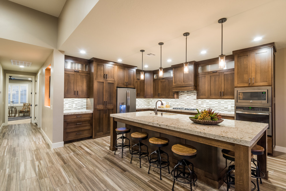 Photo of a large country l-shaped open plan kitchen in Salt Lake City with shaker cabinets, dark wood cabinets, granite benchtops, grey splashback, matchstick tile splashback, stainless steel appliances, porcelain floors, with island and a single-bowl sink.