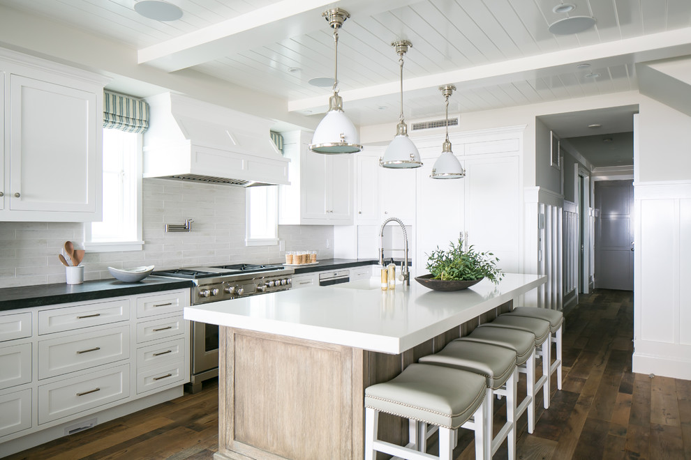 Photo of a beach style kitchen in Orange County with shaker cabinets, white cabinets, white splashback, stainless steel appliances, with island and dark hardwood floors.