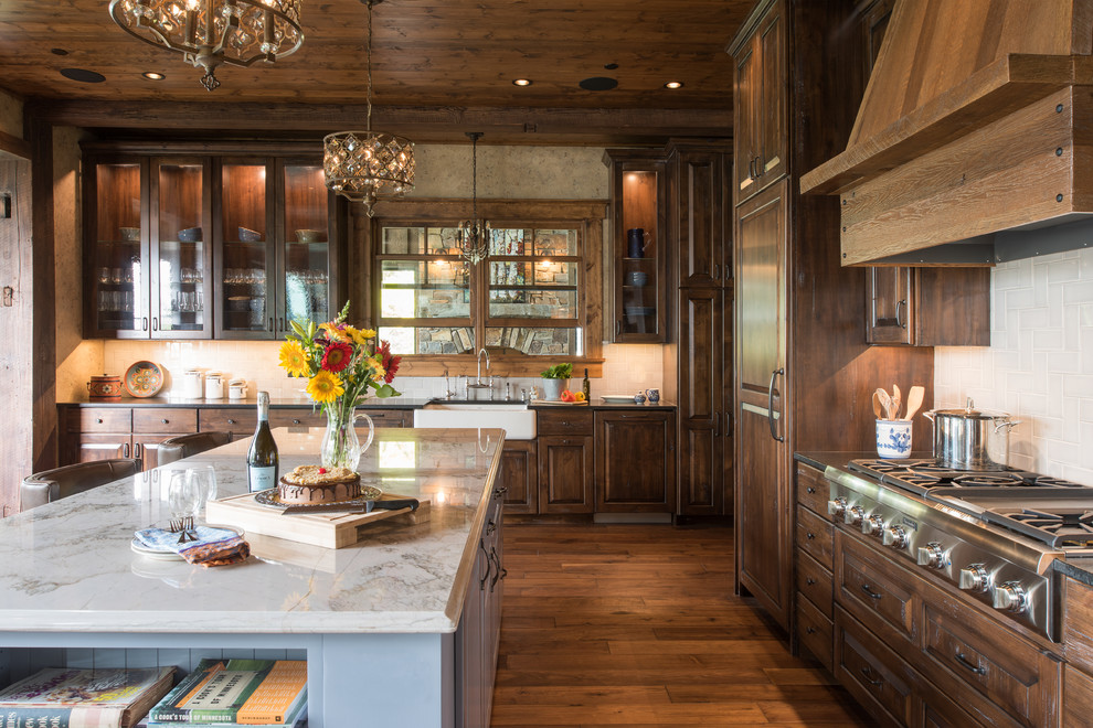 Inspiration for a country kitchen in Minneapolis with raised-panel cabinets, with island, a farmhouse sink, dark wood cabinets, white splashback, stainless steel appliances, dark hardwood floors and brown floor.