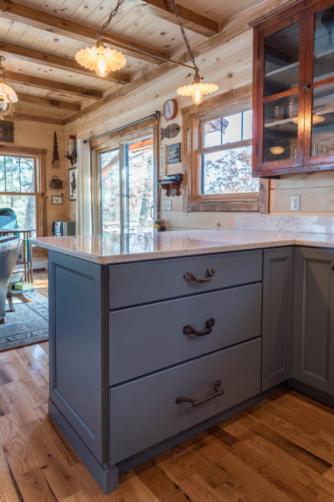 This is an example of a small country u-shaped eat-in kitchen in Minneapolis with a farmhouse sink, flat-panel cabinets, blue cabinets, quartz benchtops, white splashback, black appliances, medium hardwood floors, a peninsula, brown floor and white benchtop.