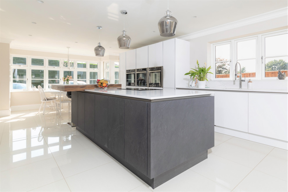 Large modern galley eat-in kitchen in Hampshire with an integrated sink, flat-panel cabinets, white cabinets, granite benchtops, white splashback, granite splashback, stainless steel appliances, ceramic floors, with island, beige floor and white benchtop.