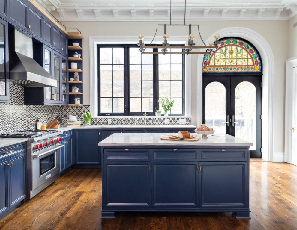 Klassisk inredning av ett stort vit vitt l-kök, med en undermonterad diskho, luckor med infälld panel, blå skåp, bänkskiva i kvartsit, flerfärgad stänkskydd, stänkskydd i mosaik, integrerade vitvaror, mörkt trägolv, en köksö och brunt golv