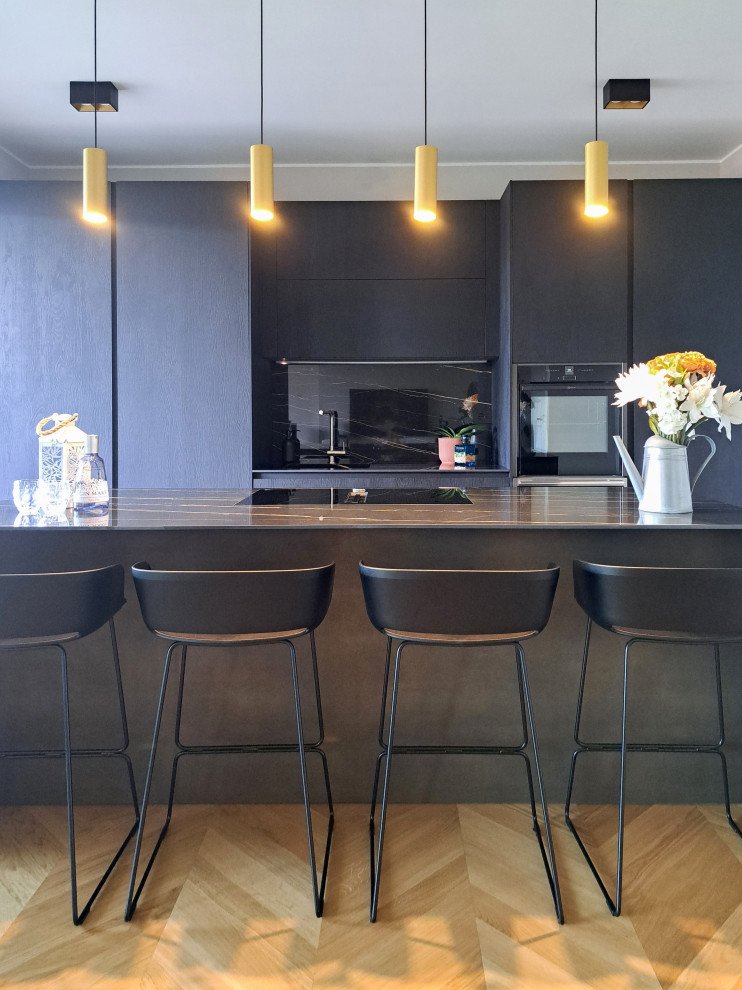 Foto di una cucina contemporanea di medie dimensioni con lavello integrato, ante nere, paraspruzzi nero, paraspruzzi in gres porcellanato, elettrodomestici neri, parquet chiaro e top nero