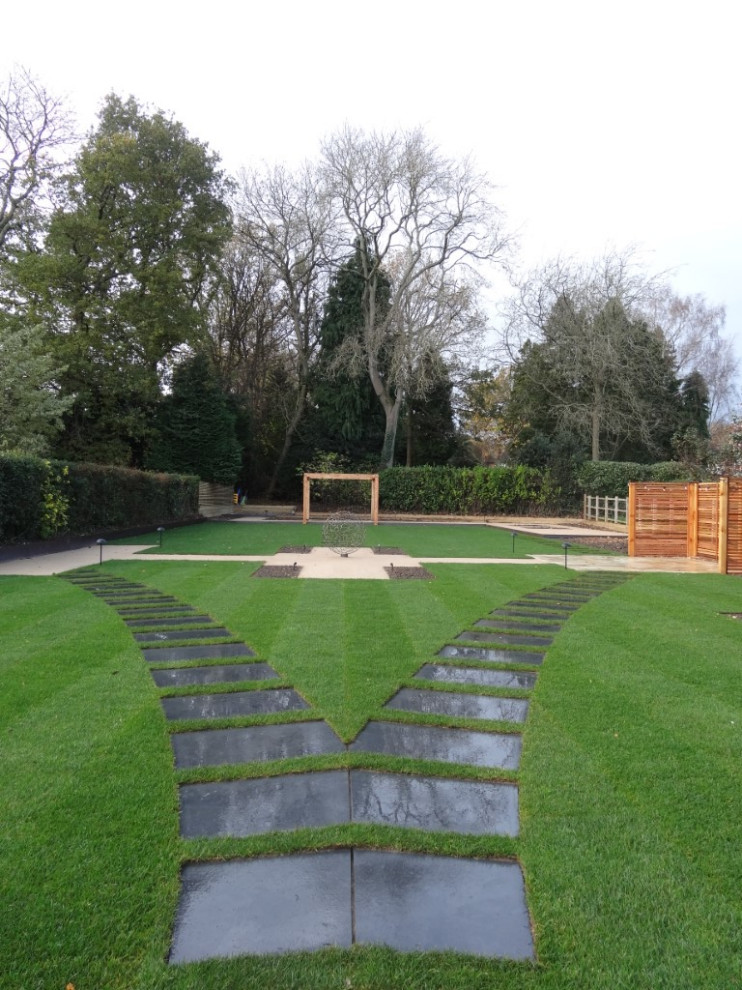 Photo of a large modern backyard full sun formal garden for summer in West Midlands with with lawn edging, natural stone pavers and a wood fence.