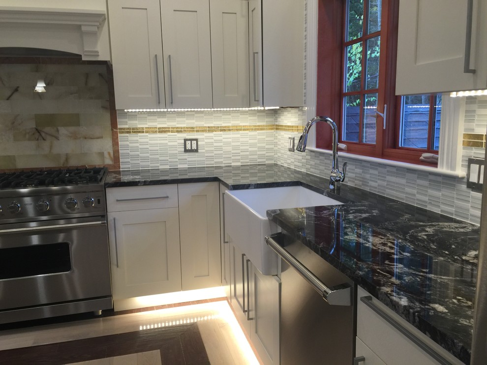 Mid-sized transitional u-shaped light wood floor and beige floor eat-in kitchen photo in Boston with white cabinets, stainless steel appliances, a farmhouse sink, granite countertops, an island, recessed-panel cabinets, beige backsplash, stone tile backsplash and multicolored countertops
