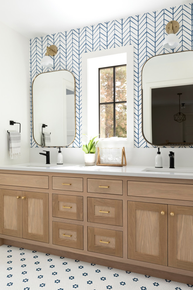 This is an example of a transitional bathroom in Minneapolis with shaker cabinets, light wood cabinets, blue walls, mosaic tile floors, an undermount sink, multi-coloured floor, white benchtops, a double vanity, a built-in vanity and wallpaper.