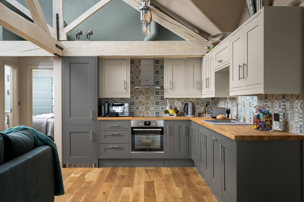 Inspiration for a large country l-shaped open plan kitchen in Gloucestershire with a drop-in sink, recessed-panel cabinets, grey cabinets, wood benchtops, stainless steel appliances, brown floor and brown benchtop.