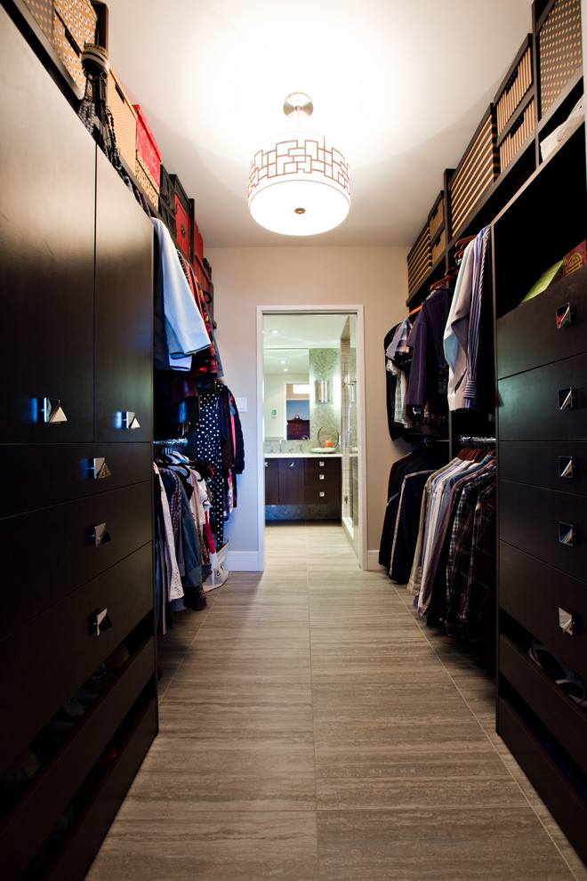 Mid-sized contemporary gender-neutral walk-in wardrobe in Other with flat-panel cabinets, dark wood cabinets and porcelain floors.