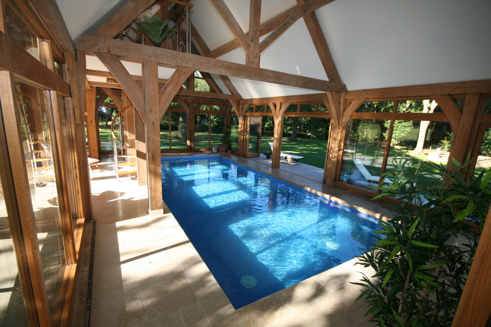 This is an example of a country indoor rectangular pool in Surrey with a pool house and natural stone pavers.