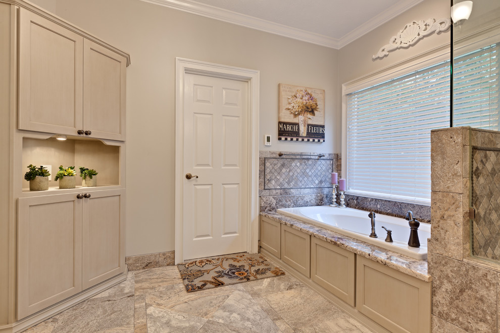 Design ideas for a large traditional master bathroom in Atlanta with recessed-panel cabinets, beige cabinets, a drop-in tub, multi-coloured tile, travertine, porcelain floors, granite benchtops, a hinged shower door, beige walls, beige floor and beige benchtops.