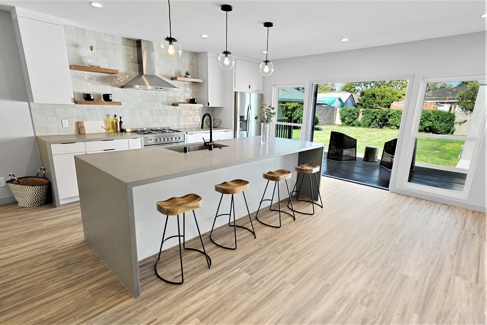 This is an example of a modern galley eat-in kitchen in Los Angeles with an undermount sink, grey splashback, stainless steel appliances, with island, flat-panel cabinets, white cabinets, quartz benchtops, porcelain splashback and grey benchtop.