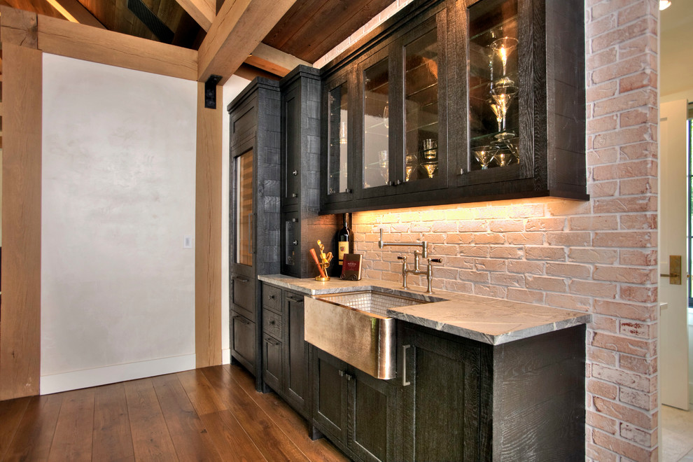 Inspiration for a mid-sized country single-wall wet bar in Other with an undermount sink, recessed-panel cabinets, black cabinets, red splashback, brick splashback, medium hardwood floors and soapstone benchtops.