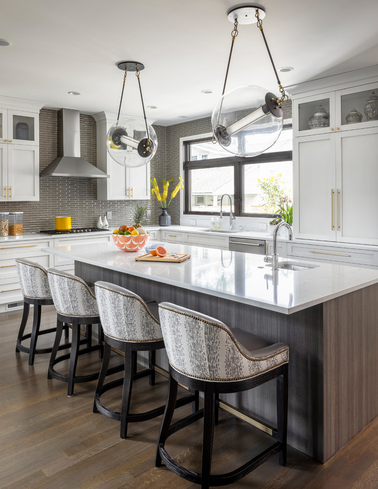Photo of a transitional l-shaped kitchen in New York with an undermount sink, shaker cabinets, white cabinets, grey splashback, matchstick tile splashback, stainless steel appliances, dark hardwood floors, with island, brown floor and white benchtop.