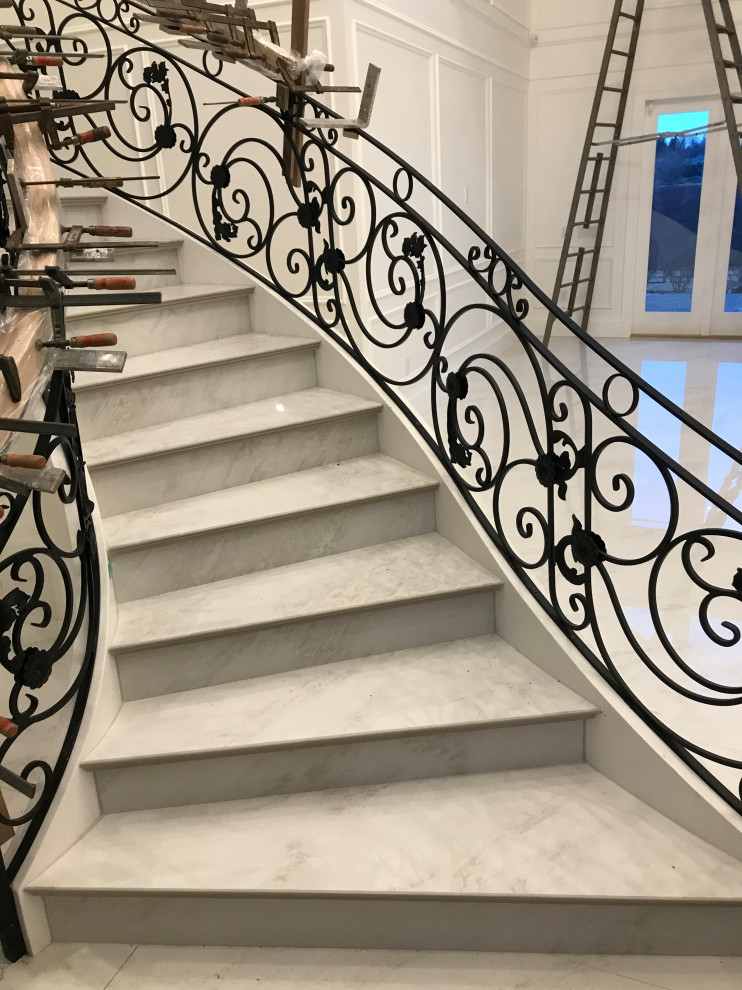 Aménagement d'un très grand escalier courbe victorien en marbre avec un garde-corps en métal, des contremarches en marbre et boiseries.
