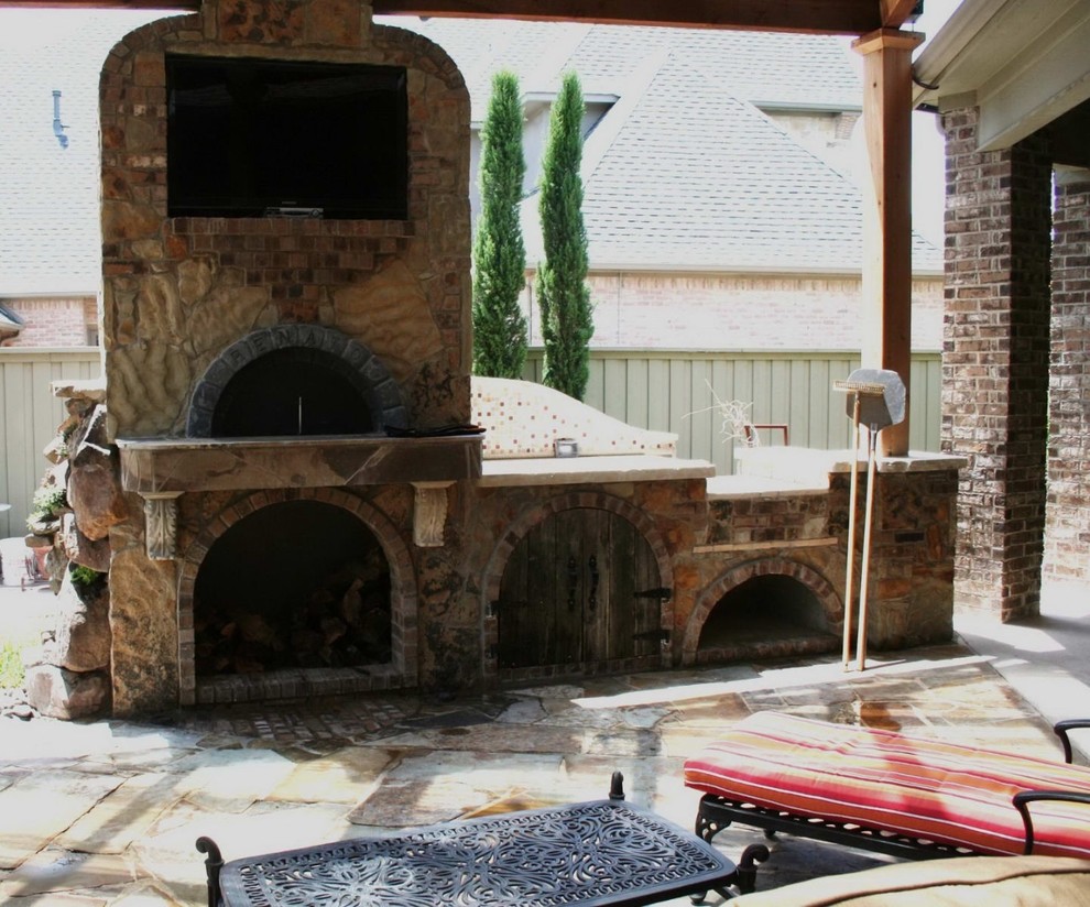 Country backyard patio in Dallas with a fire feature, natural stone pavers and a roof extension.