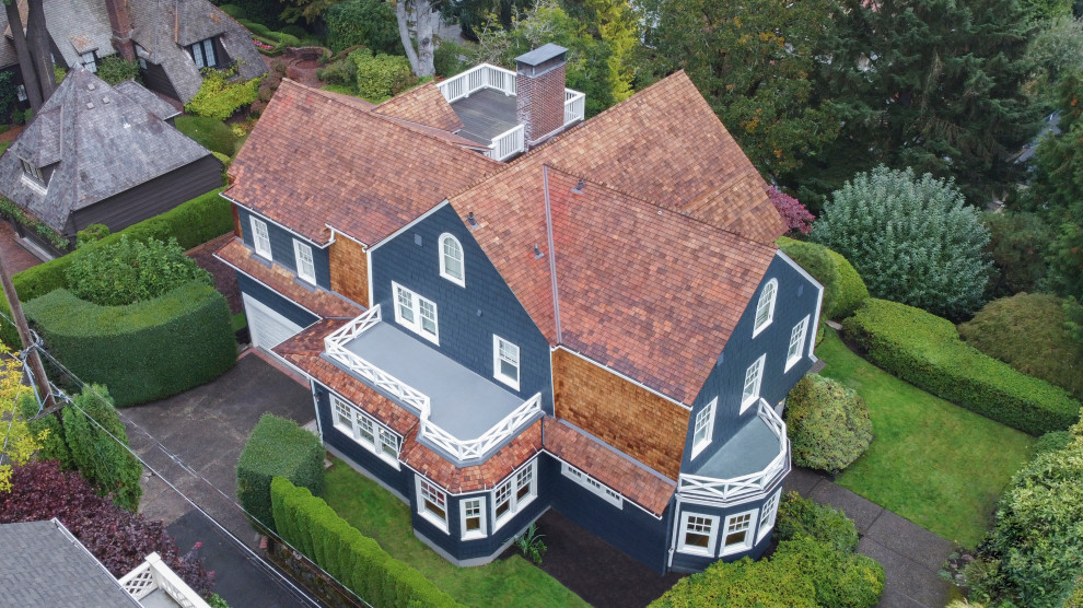 This is an example of a large traditional three-storey blue house exterior in Portland with a brown roof.
