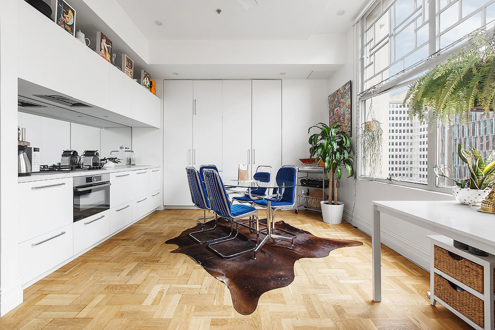 This is an example of a scandinavian eat-in kitchen in Melbourne with flat-panel cabinets, white cabinets, mirror splashback, light hardwood floors, beige floor and grey benchtop.