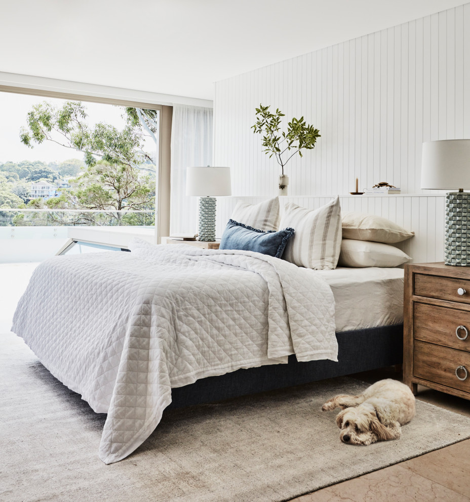 Photo of a large beach style master bedroom in Sydney with white walls, travertine floors and panelled walls.