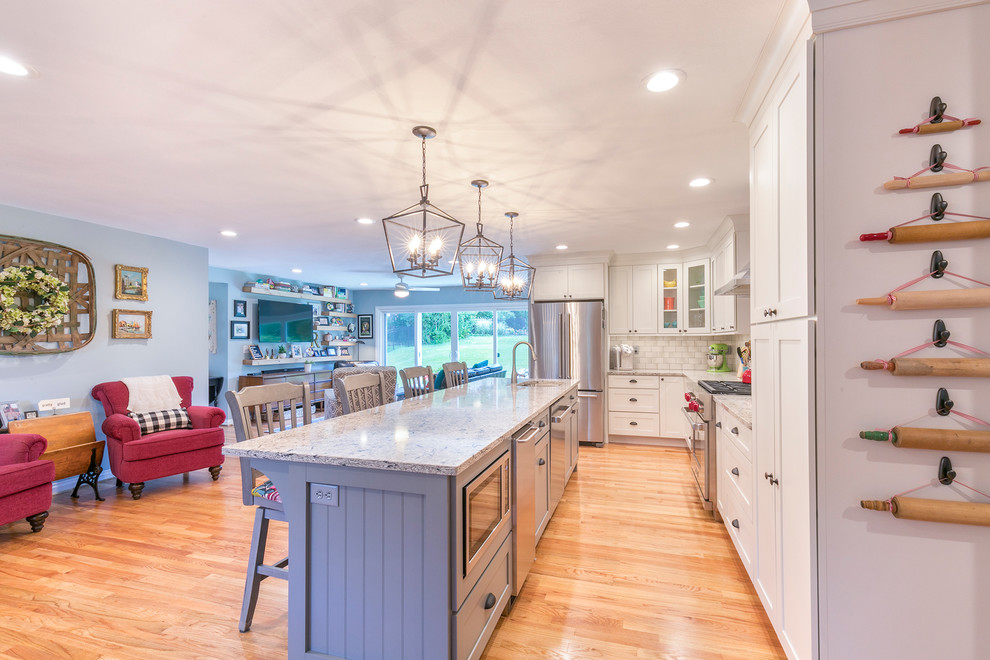 Photo of an eclectic l-shaped open plan kitchen in St Louis with an undermount sink, shaker cabinets, white cabinets, quartz benchtops, grey splashback, subway tile splashback, stainless steel appliances, medium hardwood floors, with island, brown floor and multi-coloured benchtop.