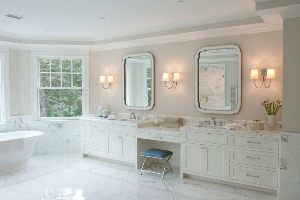 This is an example of an expansive transitional bathroom in Boston with white cabinets, a freestanding tub, an open shower, beige tile, marble, beige walls, marble floors, marble benchtops, a hinged shower door, white benchtops, an enclosed toilet, a double vanity, a built-in vanity, shaker cabinets, an undermount sink and white floor.