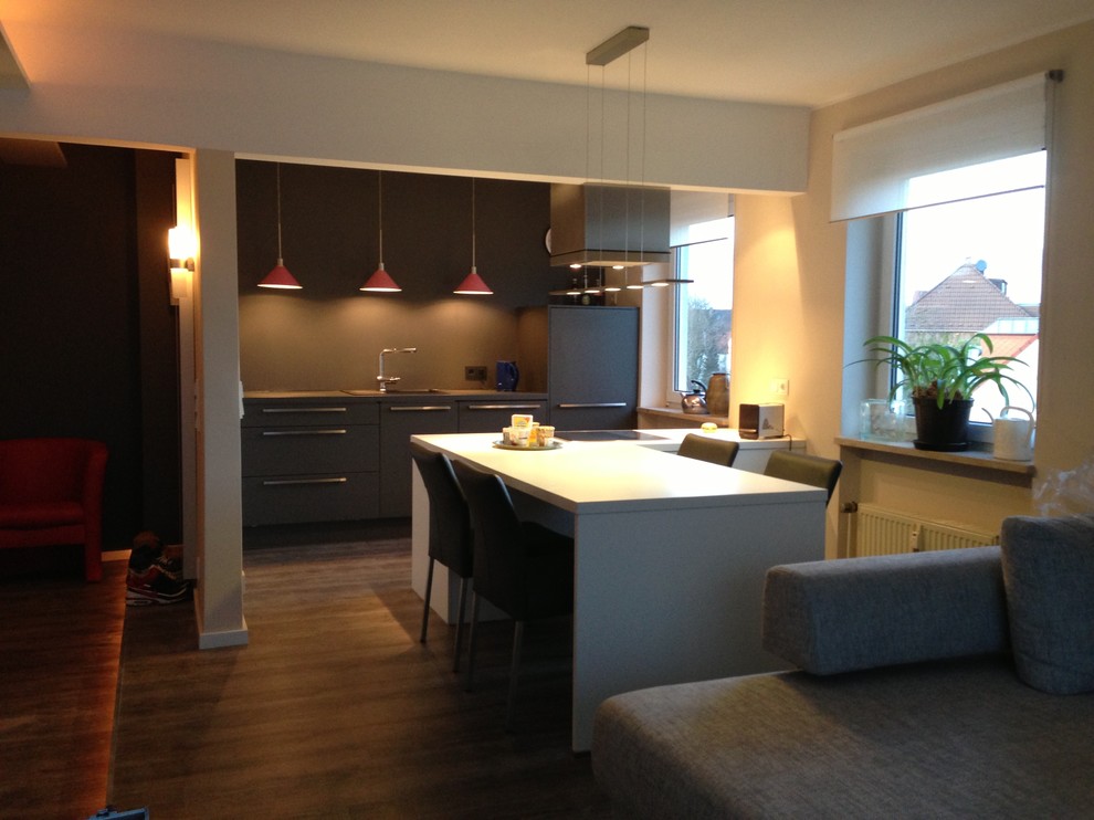 Offene, Zweizeilige Moderne Küche mit flächenbündigen Schrankfronten, schwarzen Schränken, Laminat-Arbeitsplatte, Kücheninsel, Einbauwaschbecken, Küchenrückwand in Schwarz, gebeiztem Holzboden und Elektrogeräten mit Frontblende in Essen