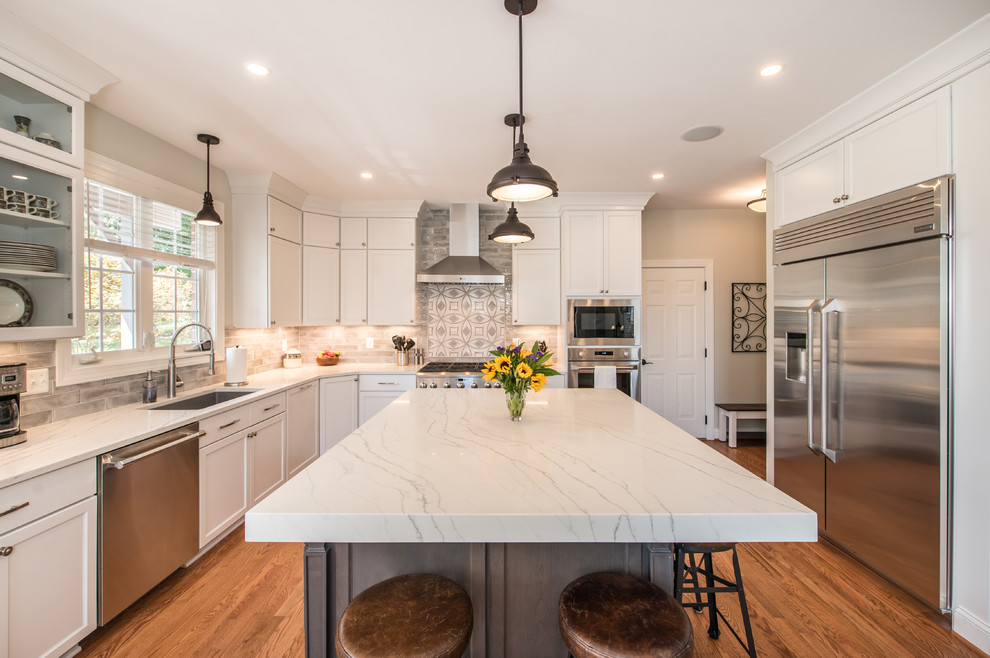 Inspiration for a large transitional u-shaped light wood floor enclosed kitchen remodel in Baltimore with an undermount sink, shaker cabinets, white cabinets, quartzite countertops, gray backsplash, ceramic backsplash, stainless steel appliances, an island and white countertops