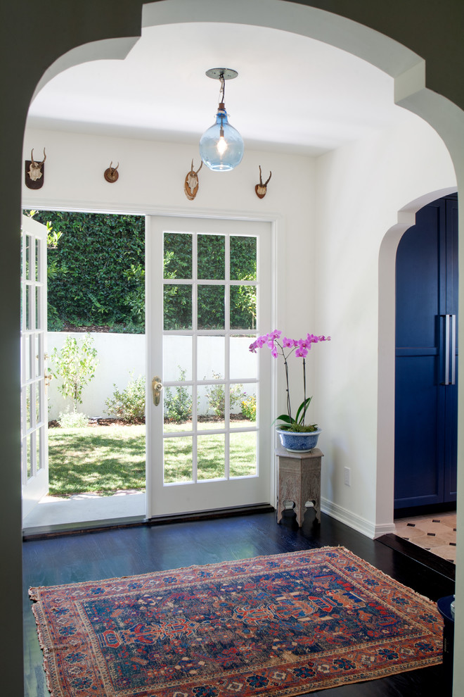 This is an example of a mid-sized mediterranean foyer in Los Angeles with white walls, dark hardwood floors, a double front door, a glass front door and black floor.