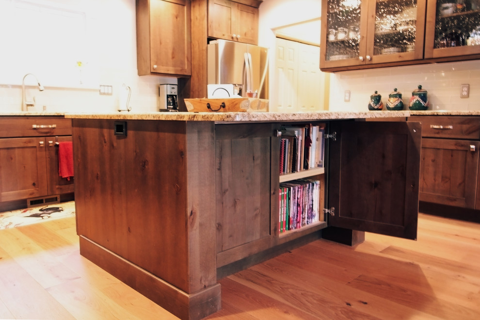 Example of a large mountain style u-shaped light wood floor and brown floor open concept kitchen design in Boise with an undermount sink, shaker cabinets, brown cabinets, granite countertops, white backsplash, glass tile backsplash, stainless steel appliances and an island
