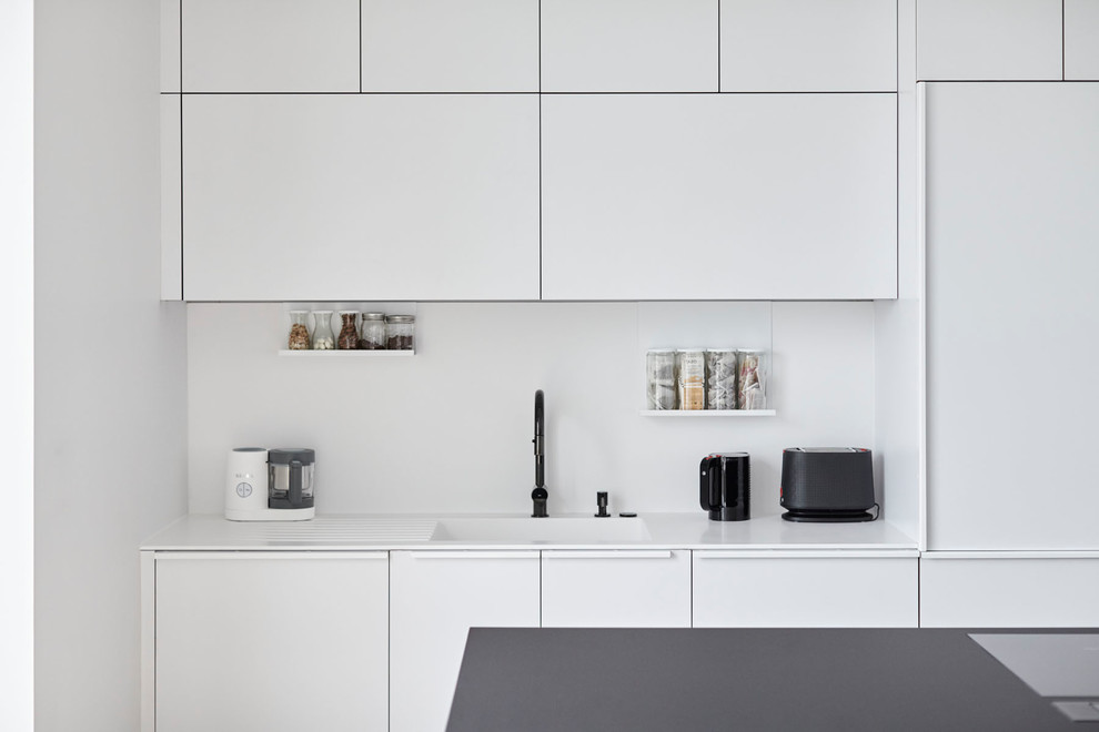 Inspiration for a small modern galley eat-in kitchen in San Francisco with an undermount sink, flat-panel cabinets, white cabinets, solid surface benchtops, white splashback, black appliances, no island and white benchtop.
