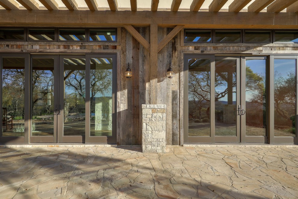 Expansive country backyard verandah in Austin with natural stone pavers and a pergola.