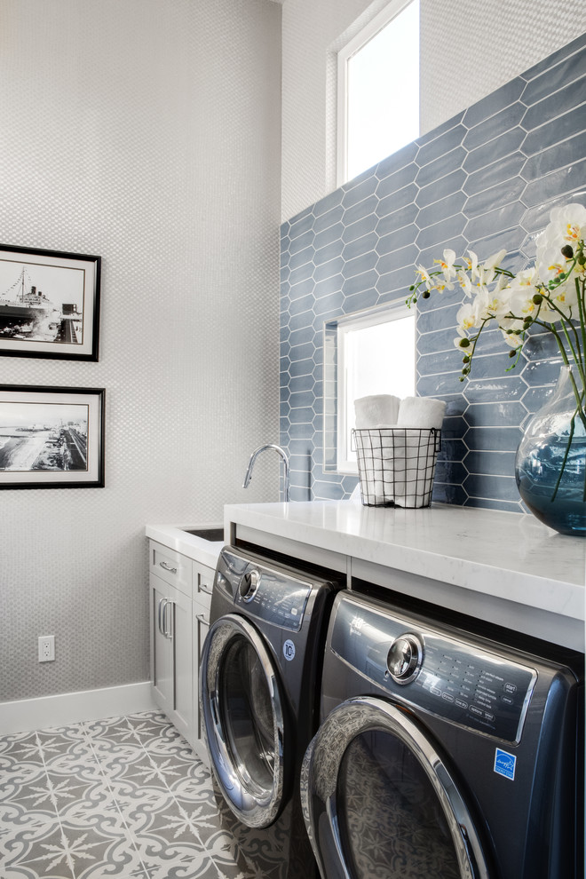 Inspiration for a mid-sized beach style galley dedicated laundry room in Los Angeles with an undermount sink, shaker cabinets, grey cabinets, quartz benchtops, grey walls, porcelain floors, a side-by-side washer and dryer, grey floor and white benchtop.
