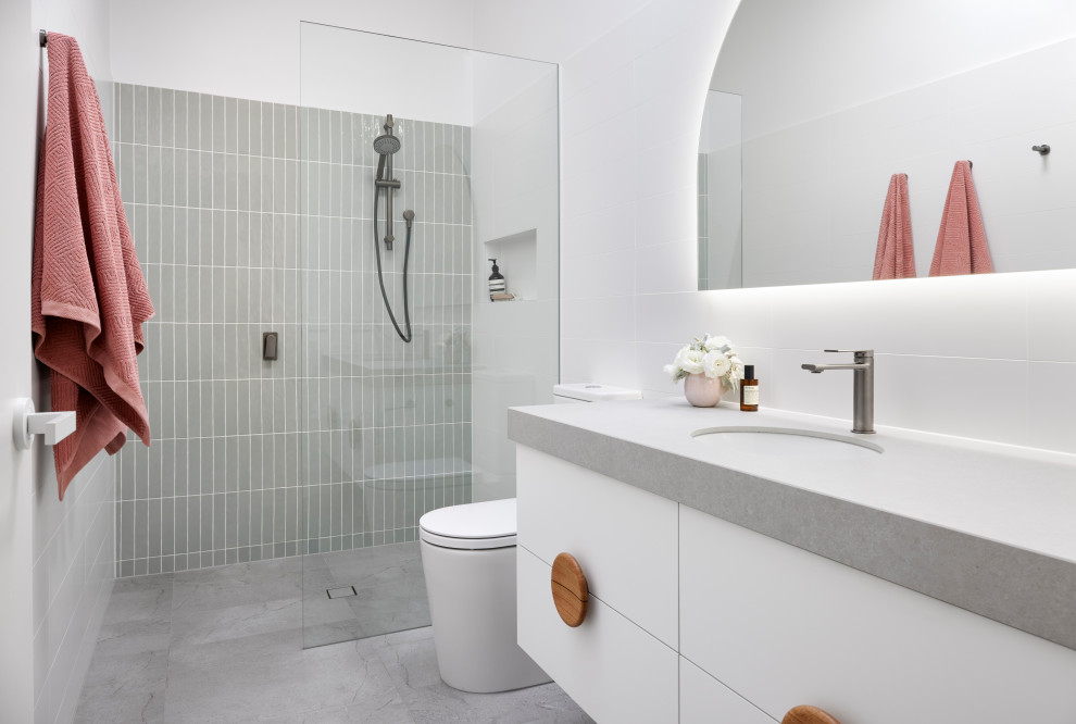 Modelo de cuarto de baño flotante contemporáneo con armarios con paneles lisos, puertas de armario blancas, ducha a ras de suelo, baldosas y/o azulejos grises, lavabo bajoencimera, suelo gris, ducha abierta, encimeras grises y hornacina