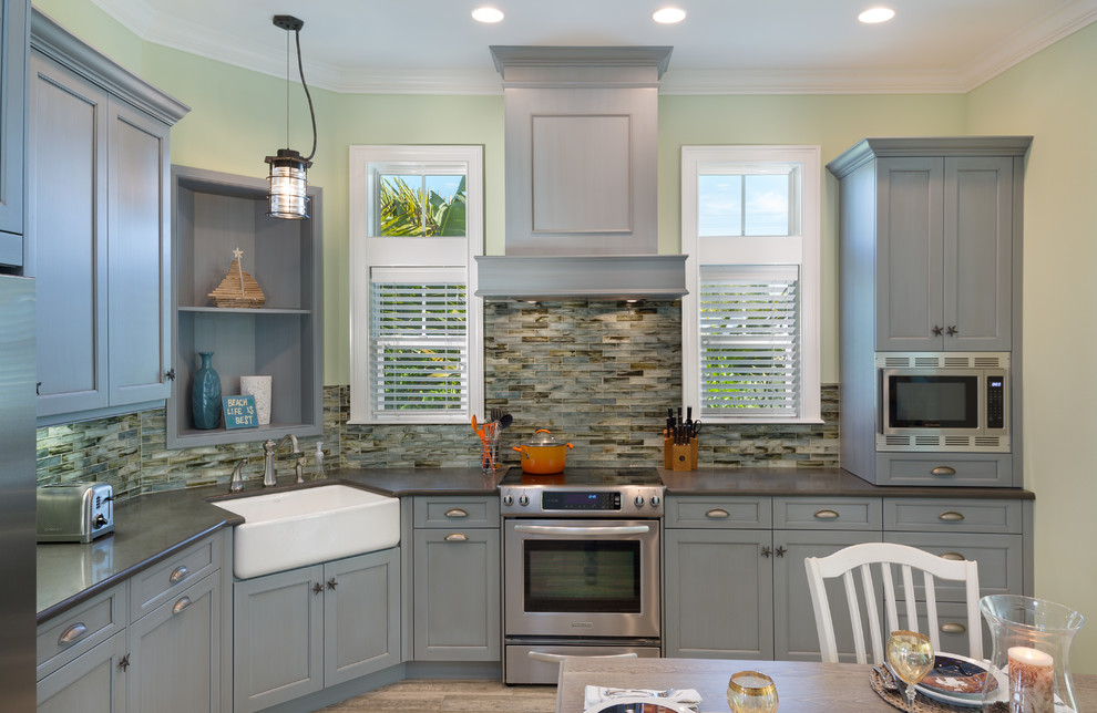 Photo of a mid-sized beach style l-shaped eat-in kitchen in Tampa with a farmhouse sink, recessed-panel cabinets, quartz benchtops, glass tile splashback, stainless steel appliances, porcelain floors, grey cabinets, black splashback and no island.