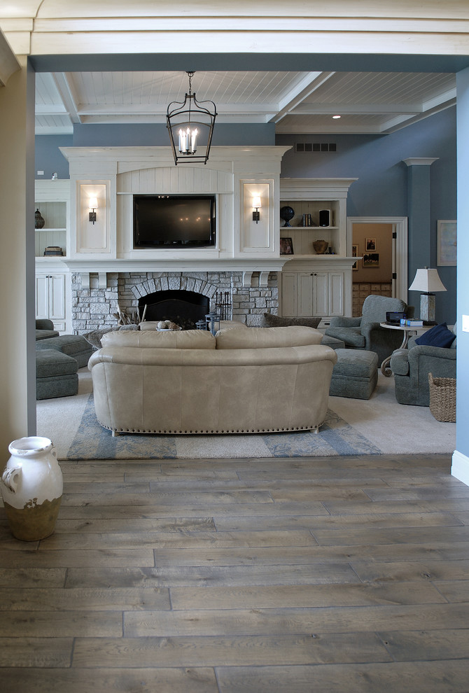 Пример оригинального дизайна: огромная гостиная комната в морском стиле с синими стенами, паркетным полом среднего тона, стандартным камином, фасадом камина из камня, мультимедийным центром, коричневым полом и сводчатым потолком