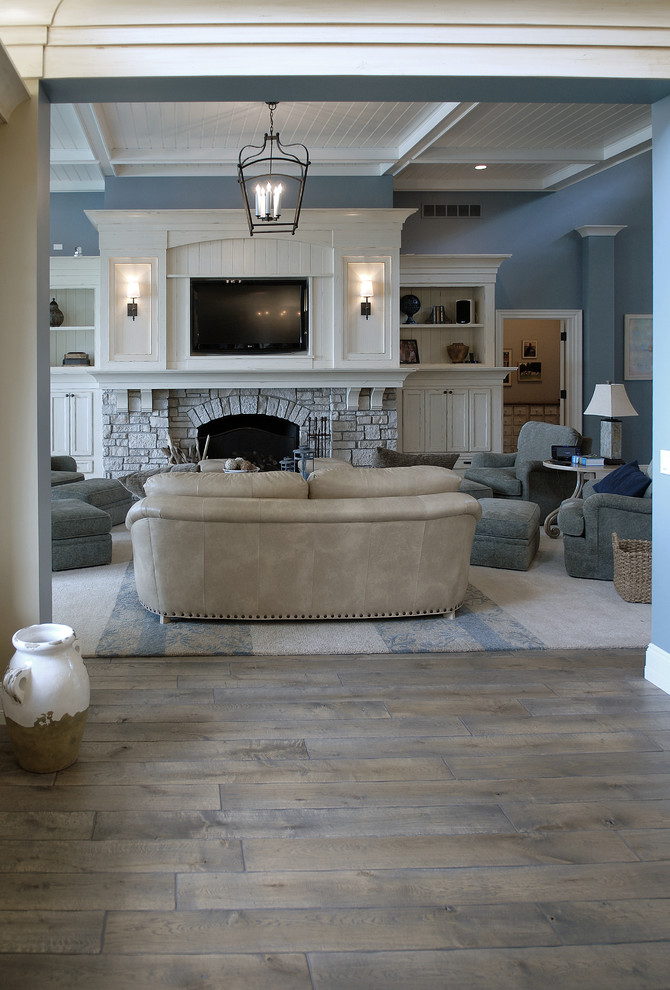 Huge beach style medium tone wood floor, brown floor and vaulted ceiling living room photo in Chicago with blue walls, a standard fireplace, a stone fireplace and a media wall