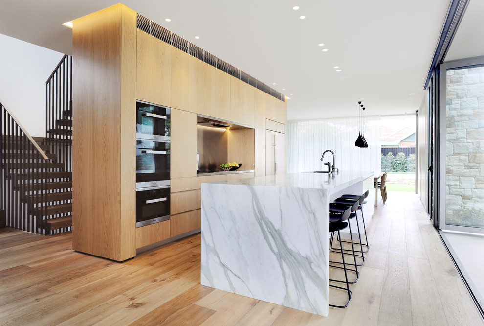 Contemporary kitchen in Sydney with black appliances, light hardwood floors and with island.